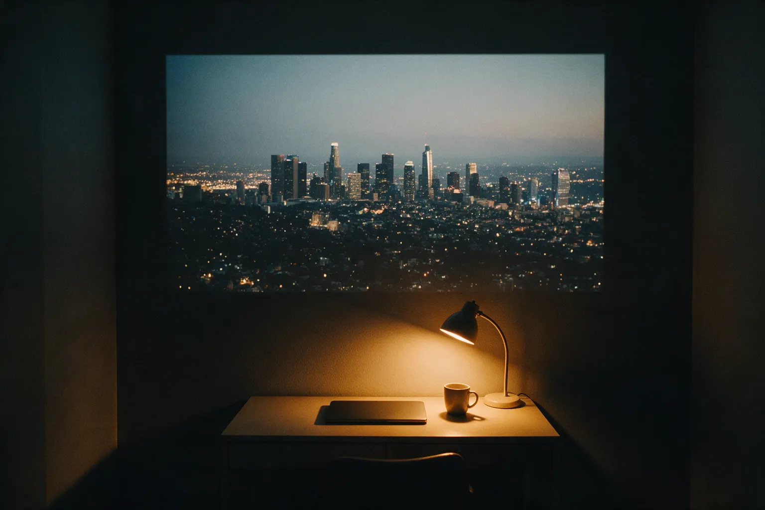 Illustrative study nook at night: a lamp-lit desk with a closed laptop and a mug under a projected city skyline
